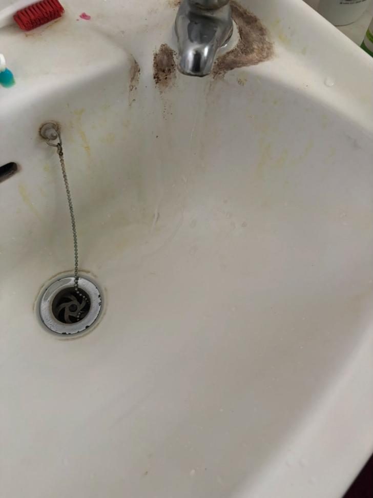 Bathroom basin with limescale and dark staining around the tap before cleaning