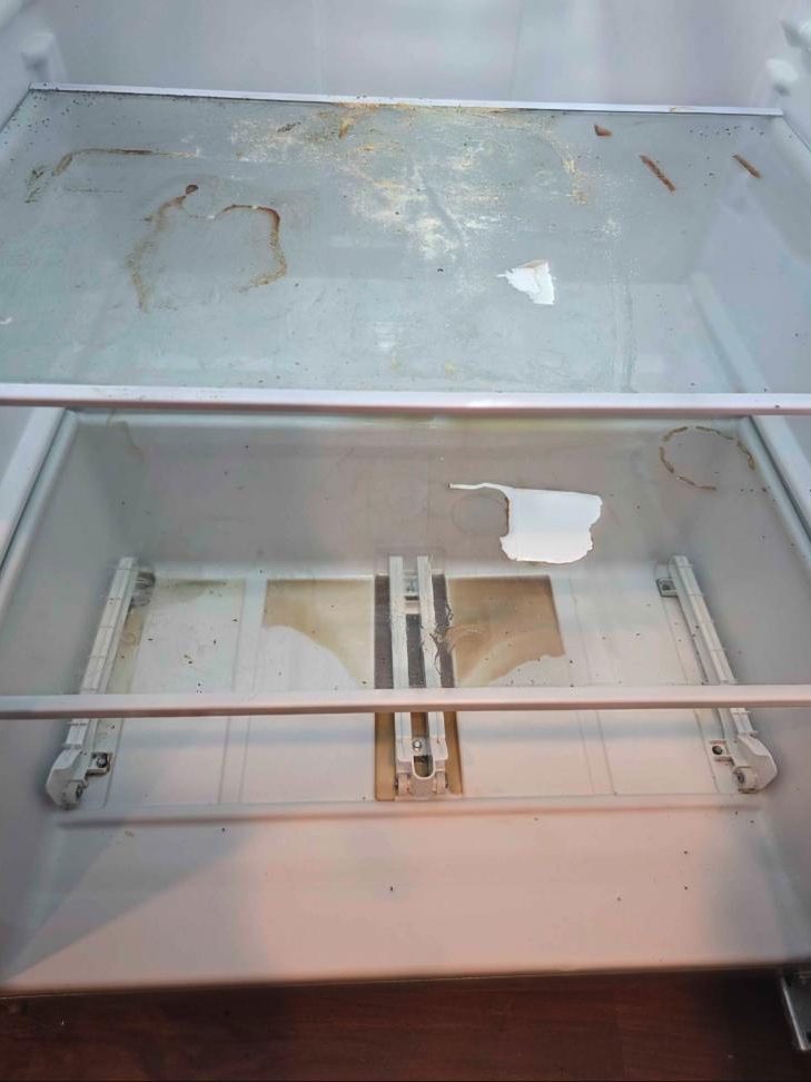 Inside of a fridge with spills and stains on the shelves before cleaning